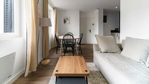 A modern living room with a sofa, a wooden coffee table, and a dining area with chairs and a table.