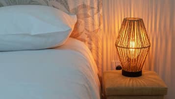 Cama com roupa de cama branca e mesa de cabeceira com abajur de tecido.