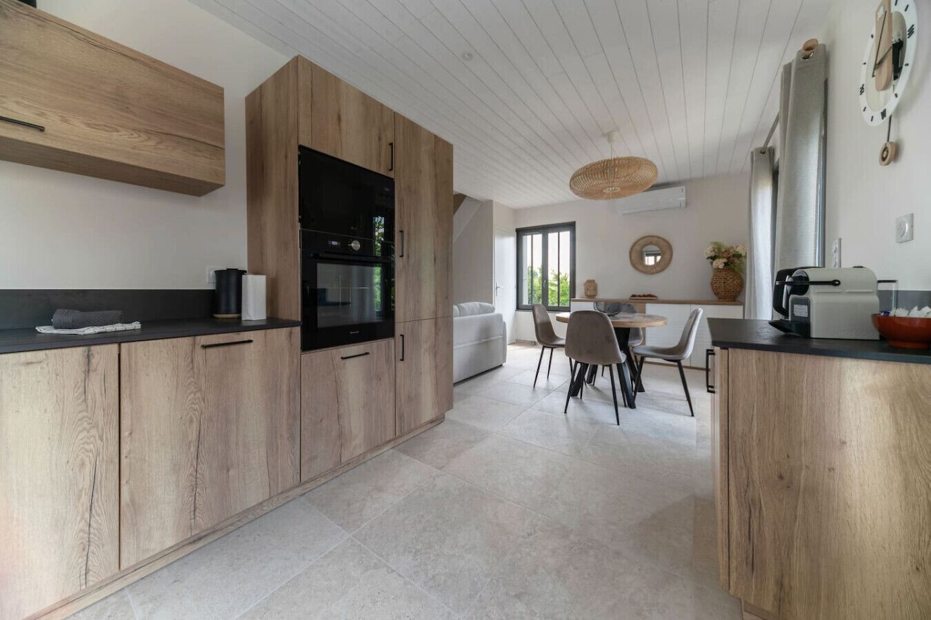 Une cuisine moderne avec des meubles en bois, un four encastré et un coin repas comprenant une table ronde et des chaises.