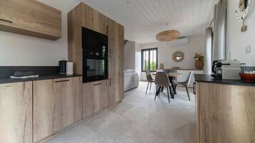 Une cuisine moderne avec des meubles en bois, un four encastré et un coin repas comprenant une table ronde et des chaises.