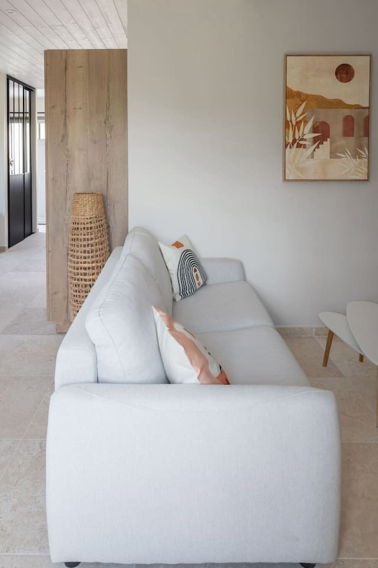 Un salon moderne avec un canapé blanc, un panier en osier et un tableau accroché au mur.