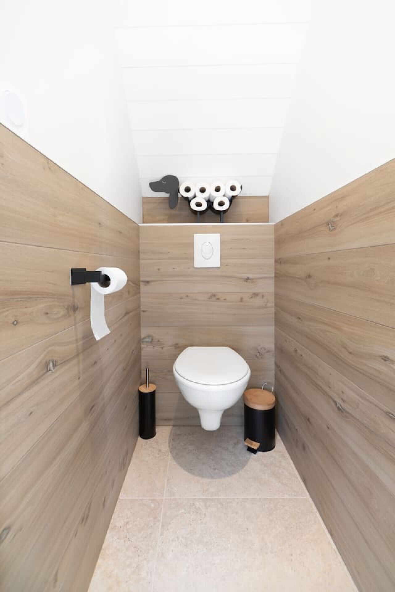 A modern bathroom with a wooden wall design, a toilet, a bidet, and a toilet paper holder.