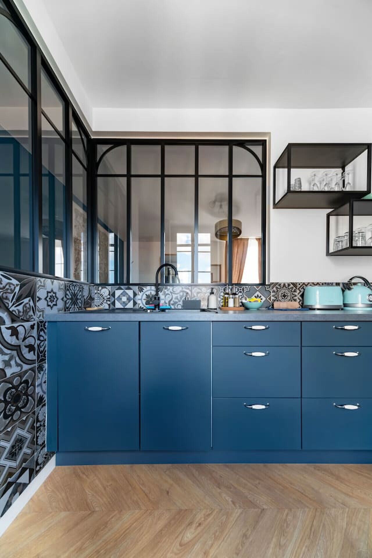Une cuisine moderne avec des armoires bleues, un dosseret à motifs et un plancher en bois.