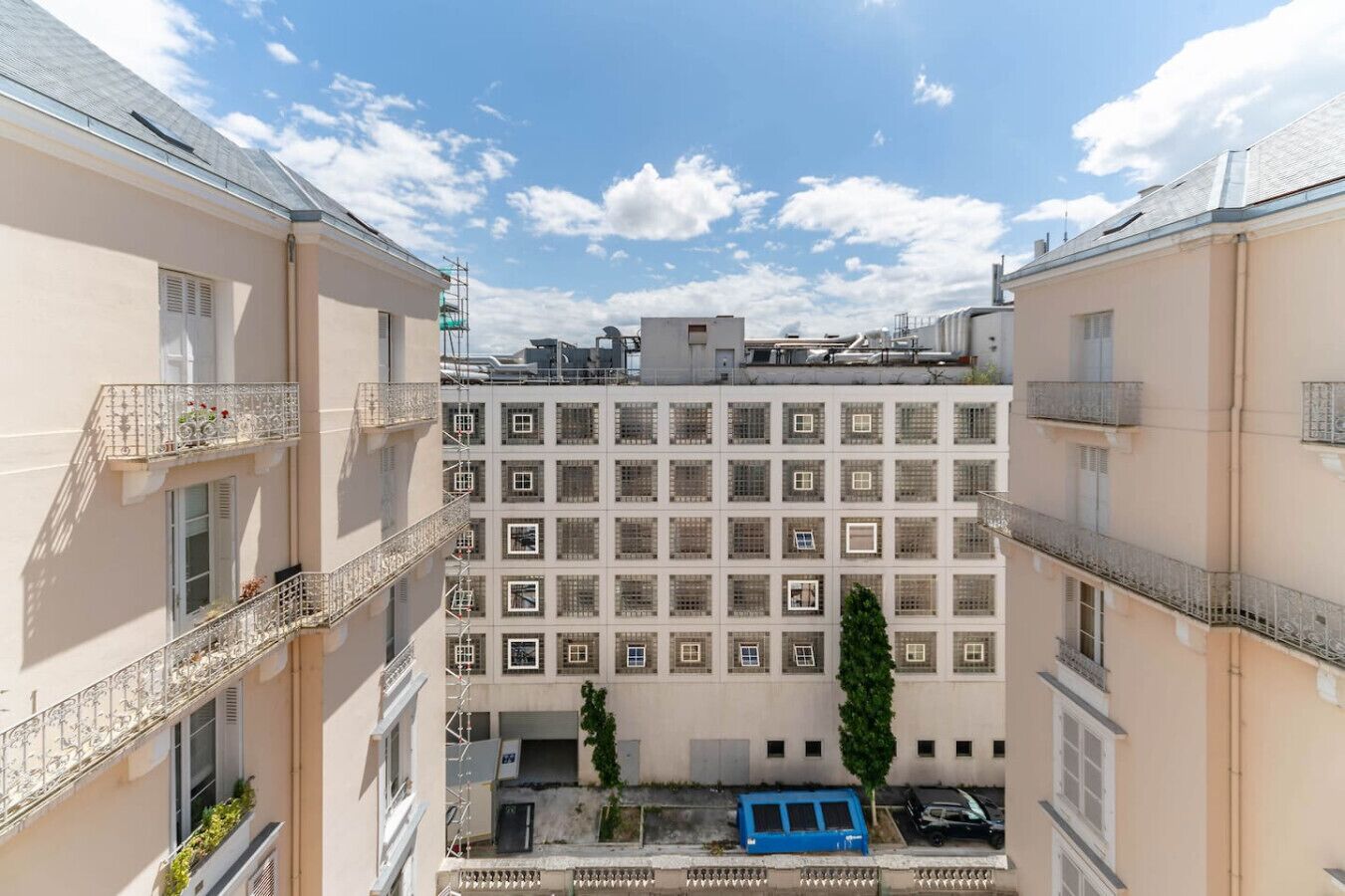 A multi-story building with a central courtyard, featuring balconies with metal railings and a blue car parked in the courtyard.