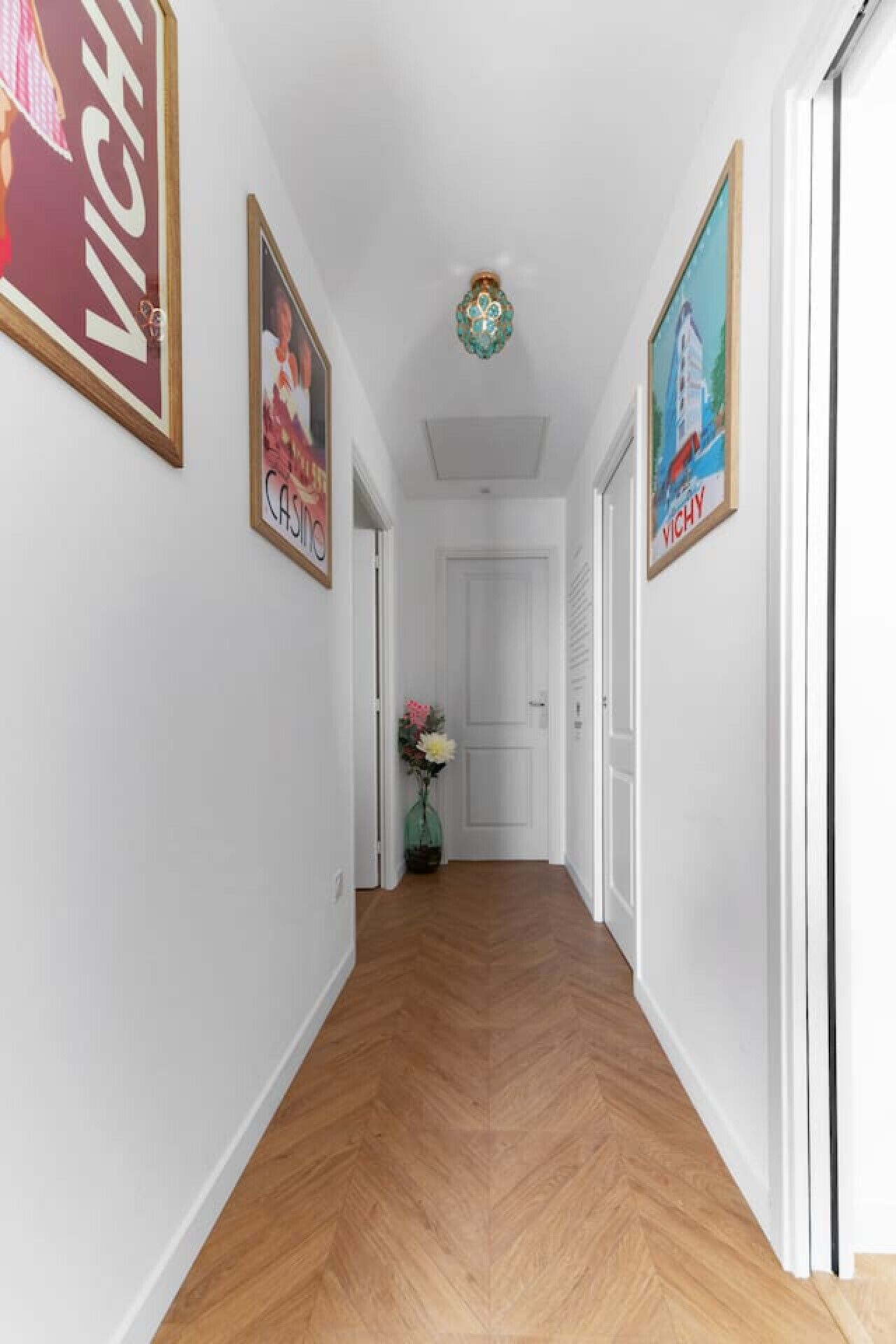 A hallway with wooden flooring, white walls, and framed pictures on the walls.