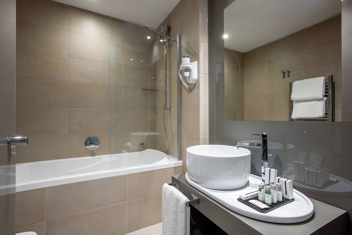 A modern bathroom with a bathtub, a round sink, and a mirror.