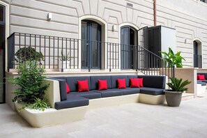 A modern outdoor seating area with a sofa, red cushions, and potted plants. - Fortyfive Squared (Rome)