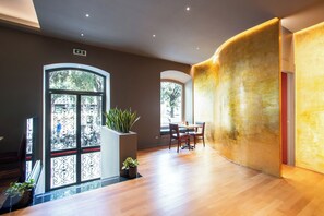 A modern interior with a wooden floor, a dining area with chairs, a large window with decorative iron, and a plant in a white planter. - Fortyfive Squared (Rome)