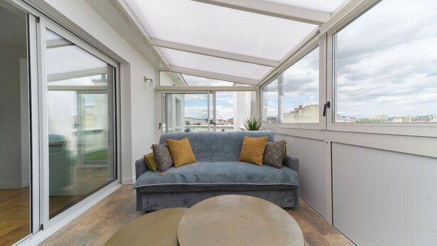 Ein modernes Wohnzimmer mit einem grauen Sofa, zwei runden Tischen und großen Fenstern mit Blick auf die Stadt.