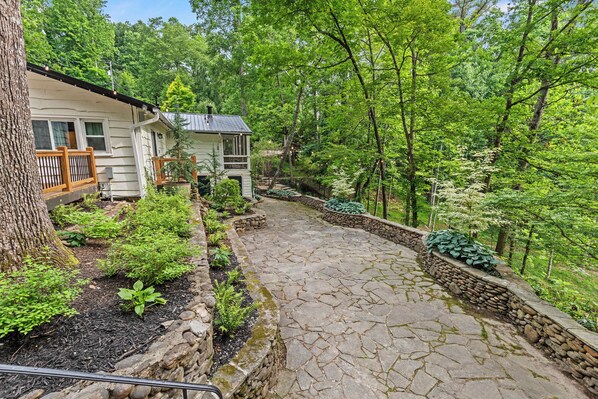 A stone pathway leading to a cabin surrounded by lush greenery and trees.