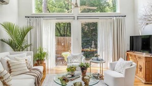 Amplio salón con una mesa de centro de vidrio grande, sofás blancos y un televisor sobre un mueble de madera.