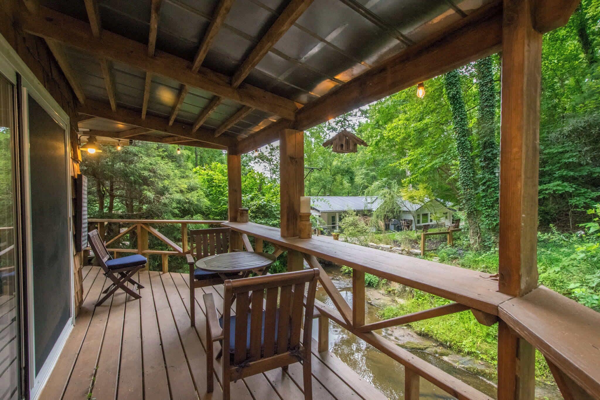 Une terrasse en bois avec une table et des chaises, donnant sur une zone boisée et une maison.