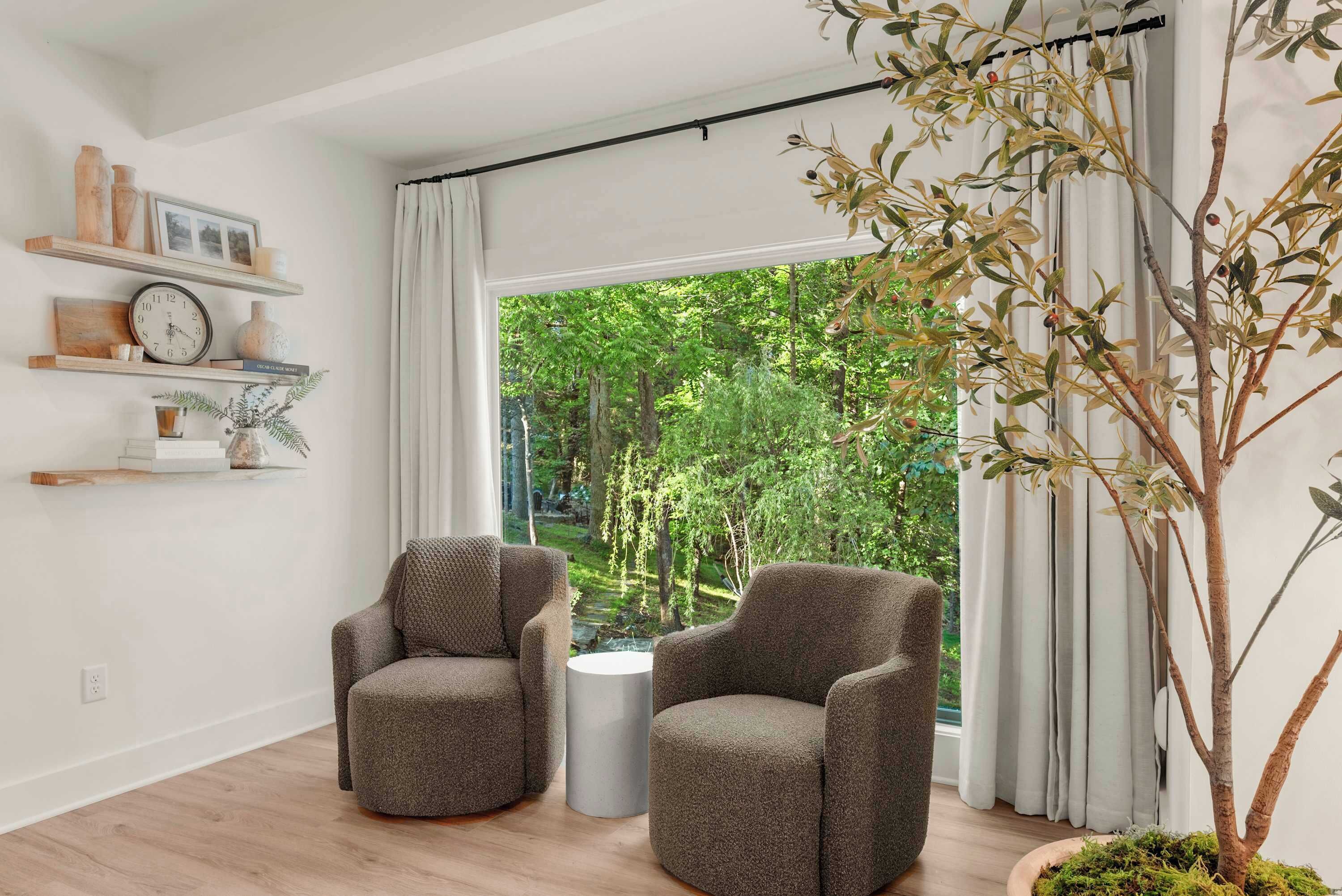 A room with two armchairs, a small round table, a clock, and shelves with decorative items.