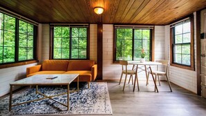 A cozy room with a wooden ceiling, large windows, a sofa, a table, and chairs. - Stone & Timber Studio Into the Woods Near Downtown (Hendersonville)