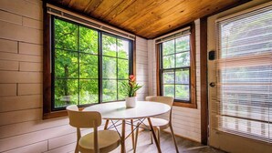 A room with a wooden ceiling, large windows with a view of greenery, a round table with chairs, and a door with blinds. - Stone & Timber Studio Into the Woods Near Downtown (Hendersonville)