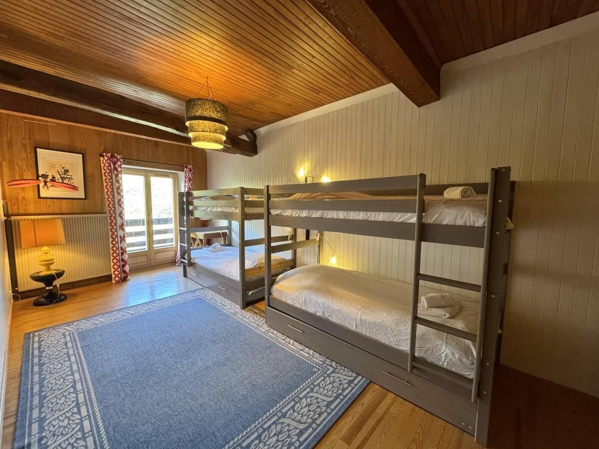 Een kamer met stapelbedden, een kamerbreed tapijt met een patroon, een lamp en een raam met gordijnen.