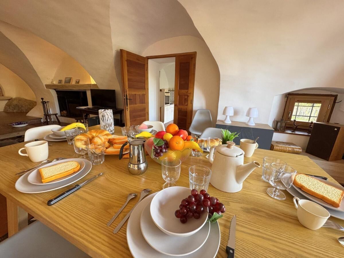 Une table de petit-déjeuner avec une table en bois, des assiettes, du pain, des fruits et une théière.