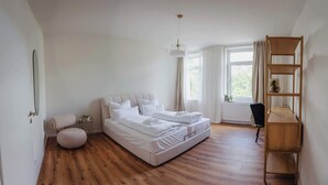 Ein Schlafzimmer mit einem großen Bett, einem Schreibtisch, einem Stuhl, einer Pendelleuchte und einem Fenster mit Vorhängen.