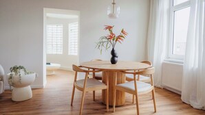 Ein moderner Essbereich mit einem runden Holztisch, vier Stühlen und einer Vase mit roten Blumen.