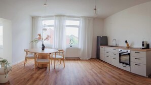 Eine moderne Küche mit weißen Schränken, einer Holz Arbeitsplatte und einem eingebauten Backofen. Es gibt eine Essecke mit einem runden Tisch und Stühlen, sowie ein Fenster mit weißen Vorhängen.