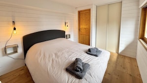 A bedroom with a large bed, two bedside lamps, a wooden door, and a window.