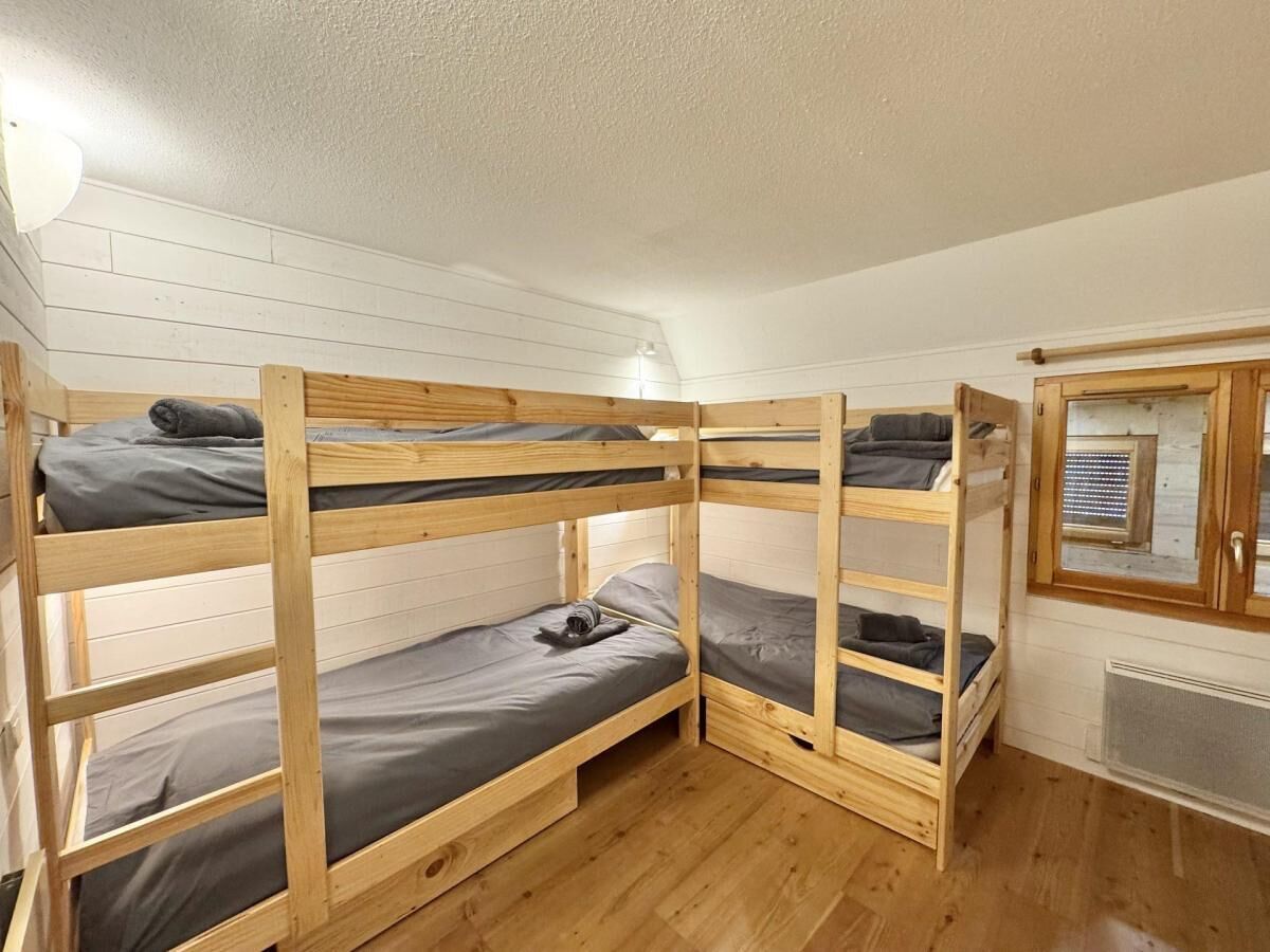 Une chambre avec des lits superposés, aux murs blancs et au plancher en bois.