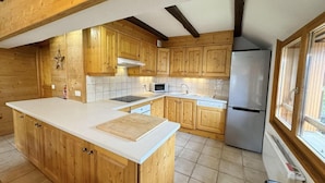 A kitchen with wooden cabinets, a stainless steel refrigerator, a microwave, and a large island with a cutting board.