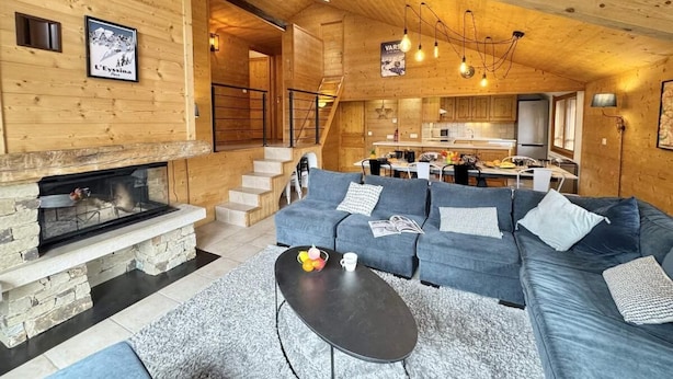 A cozy wooden interior with a stone fireplace, a blue sofa set, and a dining area.