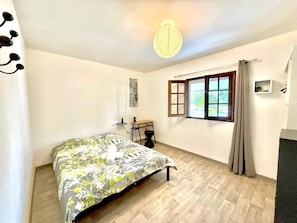 A bedroom with a bed, a desk, a chair, a window with curtains, a hanging light fixture, and a wall-mounted shelf. - Case Hermione – Mountain View in Hell-Bourg (Hell Bourg)