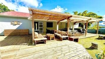 Une terrasse en bois avec des meubles d’extérieur, un espace salon couvert et un bâtiment doté d’un toit rouge.