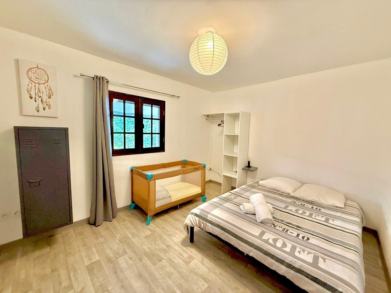A bedroom with a bunk bed, a wardrobe, a window with curtains, a bedside table, and a hanging light fixture.