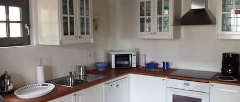 Una cocina con armarios blancos, microondas, cafetera y lavavajillas.