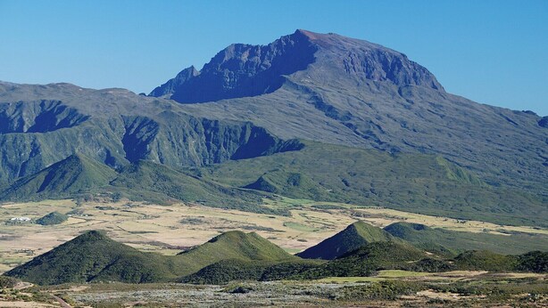 Un paisaje montañoso con un pico destacado y valles verdes.