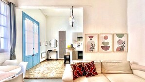Ein modernes Wohnzimmer mit einem beige farbenen Sofa, einem Esstisch mit Stühlen und einer Küche im Hintergrund.