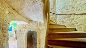 Eine steile Steintreppe führt zu einer erhöhten Ebene, vorbei an einer rustikalen Steinmauer und einem kleinen Rundbogenportal.