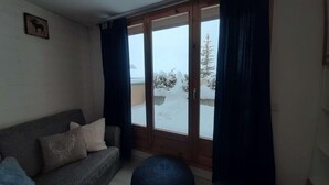 A cozy room with a sofa, a large window with curtains, and a view of a snowy landscape.