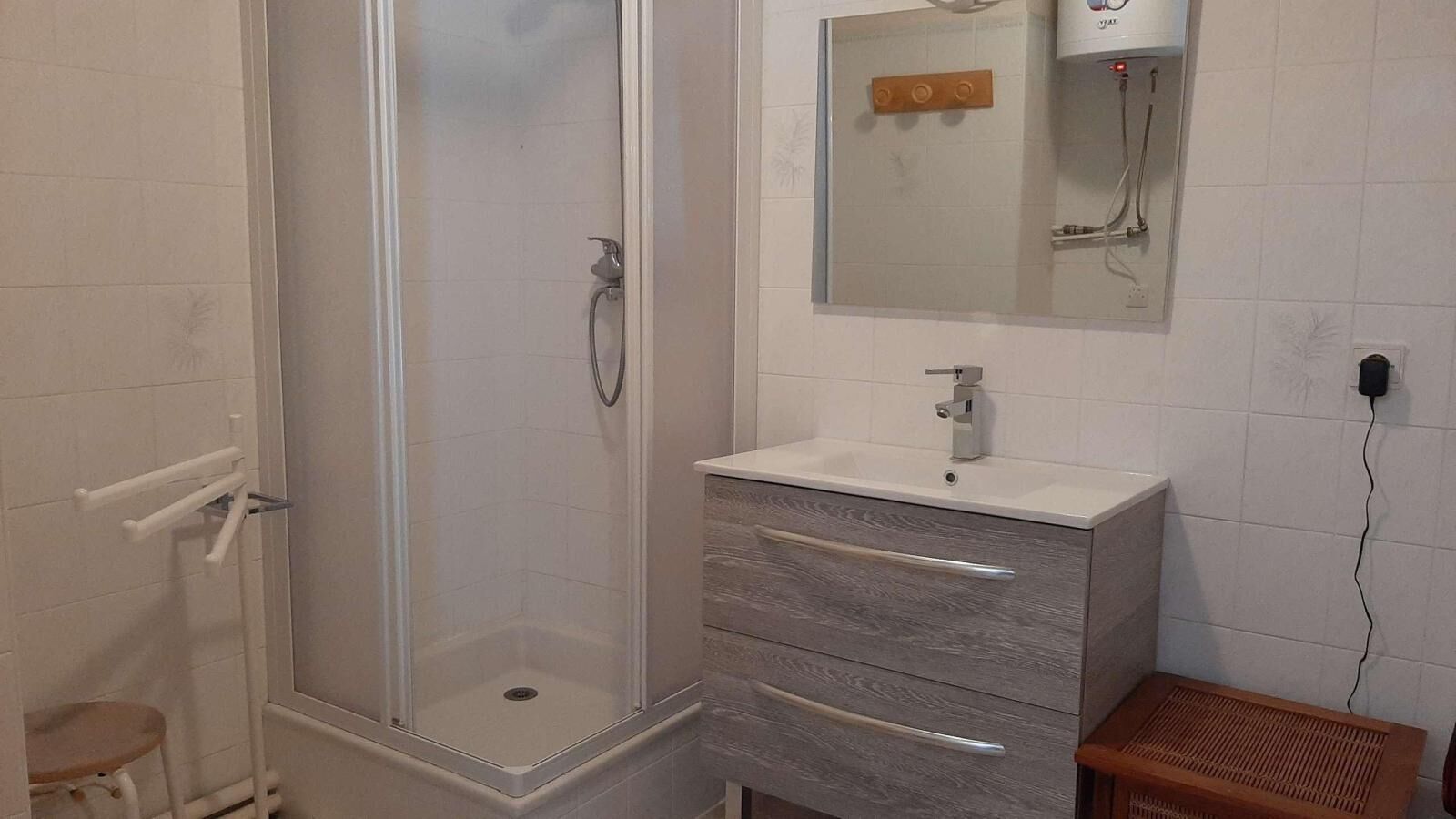 Ein Badezimmer mit einer Glaskabine zur Dusche, einem Waschtisch mit Spiegel und einem kleinen Hocker.