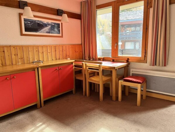 Cocina compacta con encimera de madera, armarios rojos y comedor con mesa y sillas.
