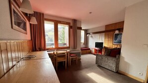 A cozy room with a wooden dining table, chairs, a sofa, and a TV. - 250m from ski slopes, 4th floor, view ski slopes, swimming pool, balcony, ski locker, 34m² (La Plagne)