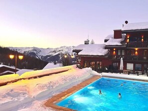Un área de piscina con alrededores nevados y montañas al fondo.
