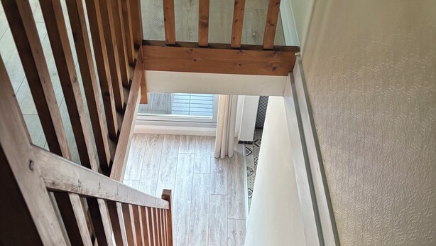 A wooden staircase leading to a room with a patterned floor and a window with blinds. - Appartement des iles (Quiberon)