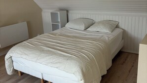 A bedroom with a bed, white headboard, and a slanted ceiling. - Appartement des iles (Quiberon)