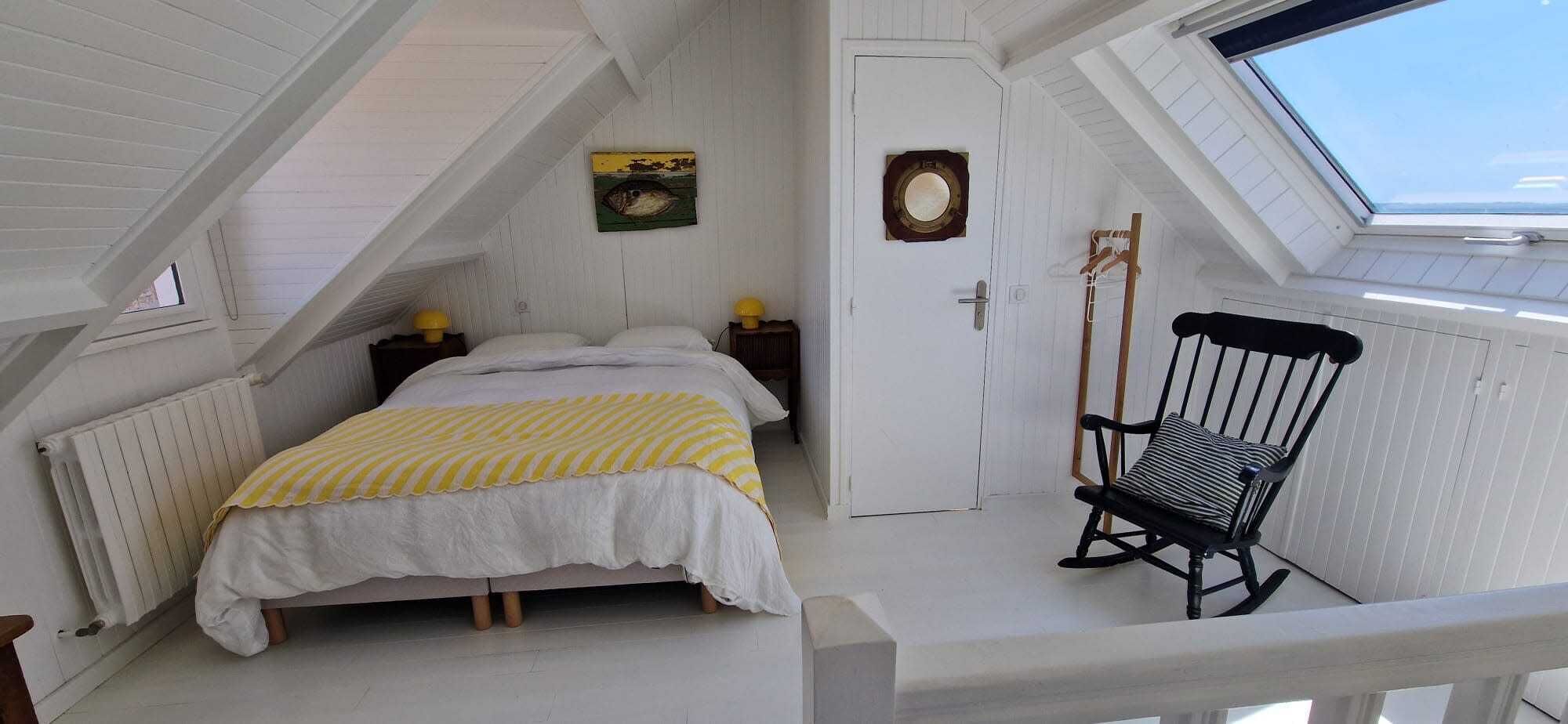 A bedroom with a bed, a rocking chair, a door, and a skylight.