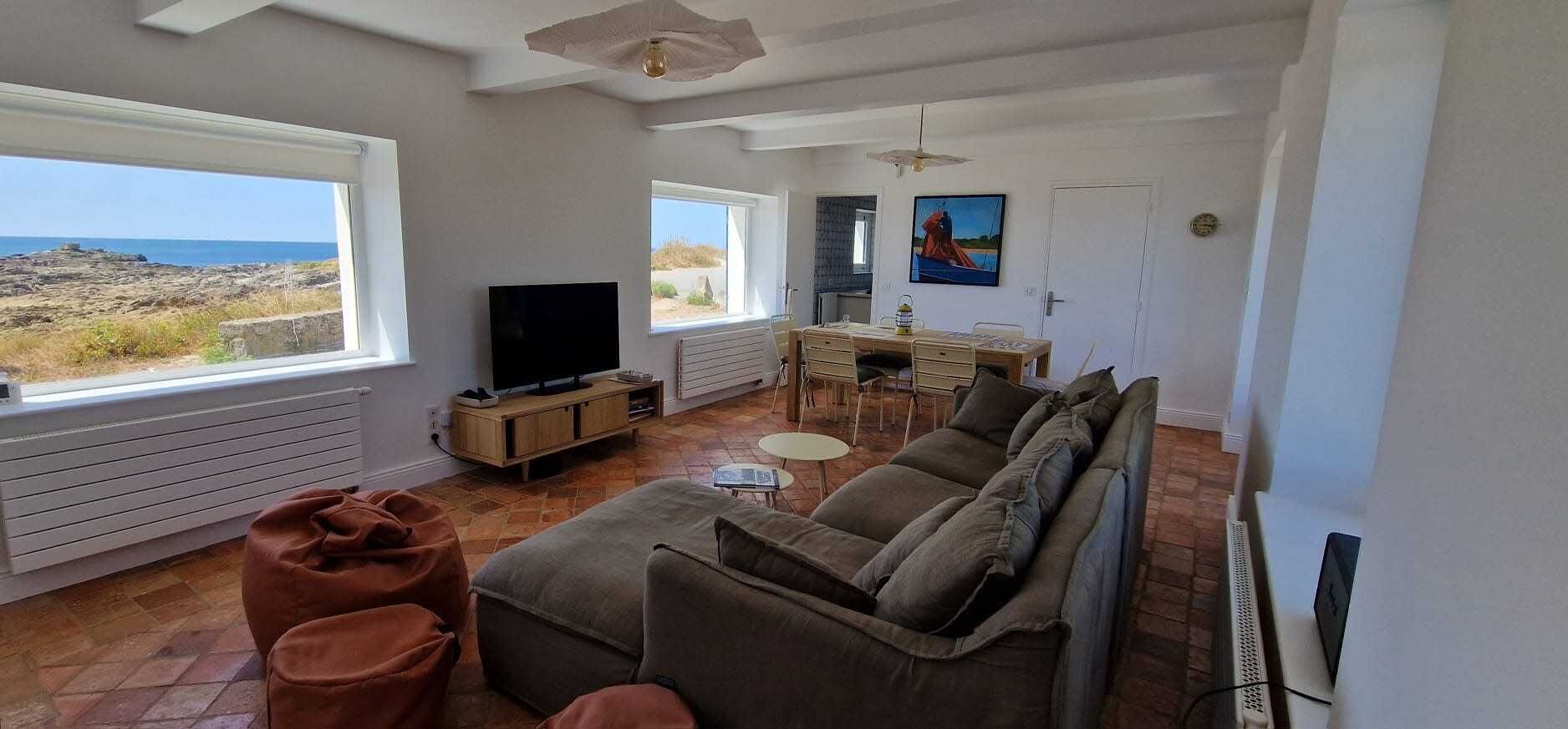 A living room with a sofa, ottoman, TV, and dining area with chairs and a table.