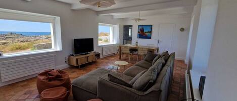 A living room with a sofa, ottoman, TV, and dining area with chairs and a table.
