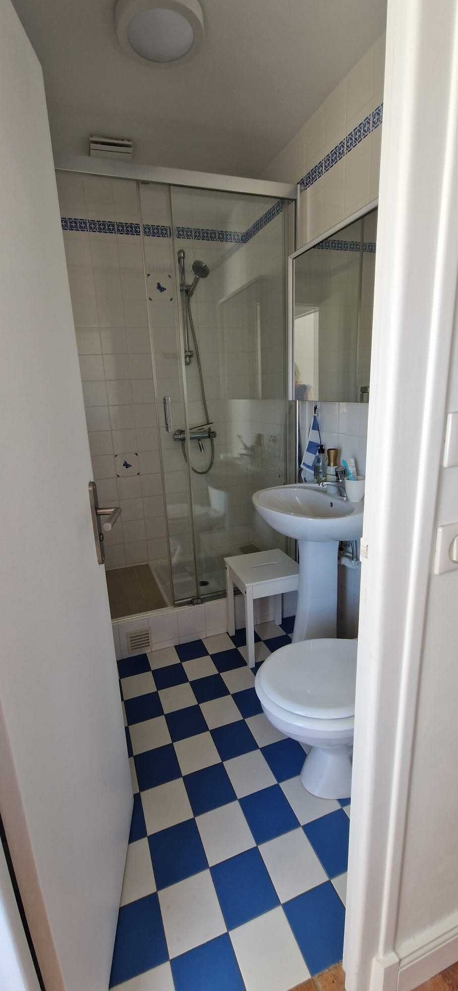 A bathroom with a checkered floor, a white sink, a toilet, and a shower area.