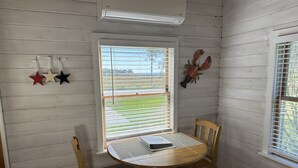 A corner room with a wooden table and chairs, a window with blinds, and a wall-mounted air conditioner. - Ocean View Dog Friendly Cottage 4-min to Kennebunkport (Kennebunk)