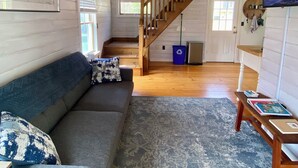 A cozy living room with a wooden staircase, a sofa, and a rug. - Ocean View Dog Friendly Cottage 4-min to Kennebunkport (Kennebunk)