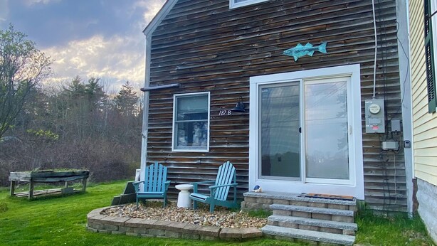 A wooden house with a large sliding glass door, a small porch with Adirondack chairs, and a mailbox marked '187 B'. - Ocean View Dog Friendly Cottage 4-min to Kennebunkport (Kennebunk)
