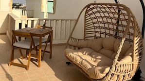 Un patio con mesa y sillas de madera, una silla colgante de mimbre y un ventilador de techo.